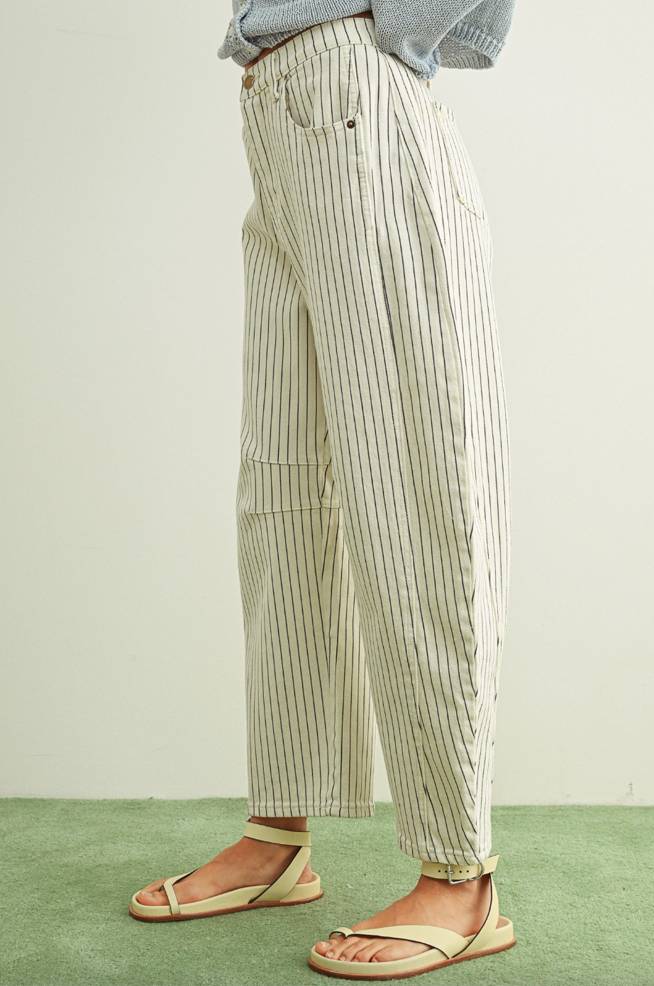 Person wearing striped pants and sandals on a green floor with a white wall background