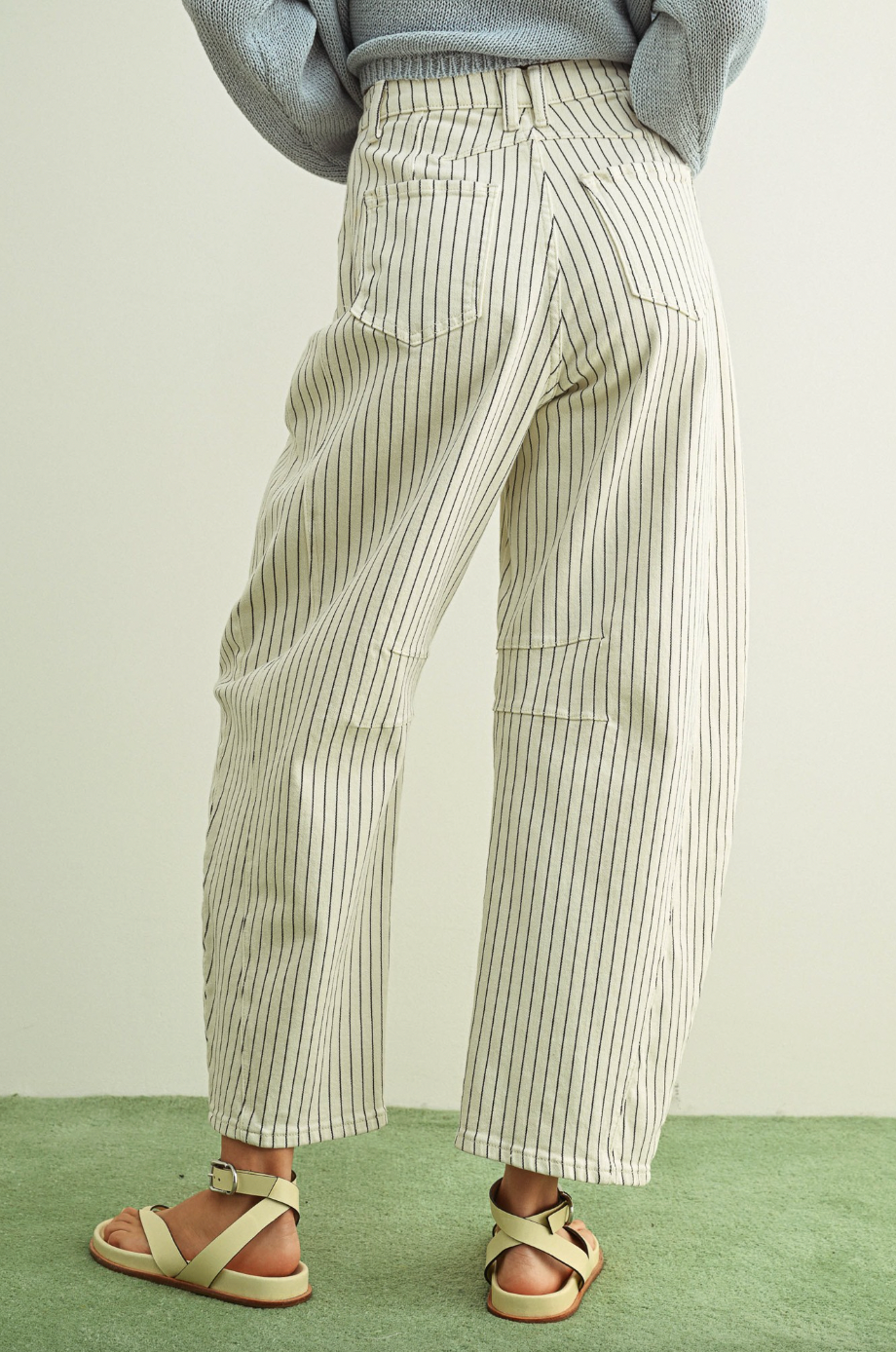Person wearing striped pants and sandals on a green floor with a light background