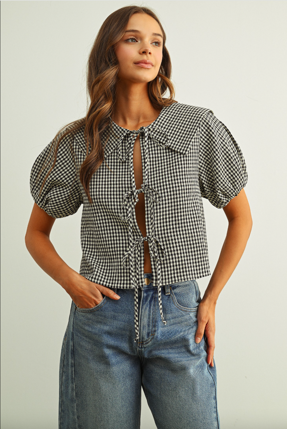 Woman wearing a checkered blouse with puff sleeves and jeans on a plain background