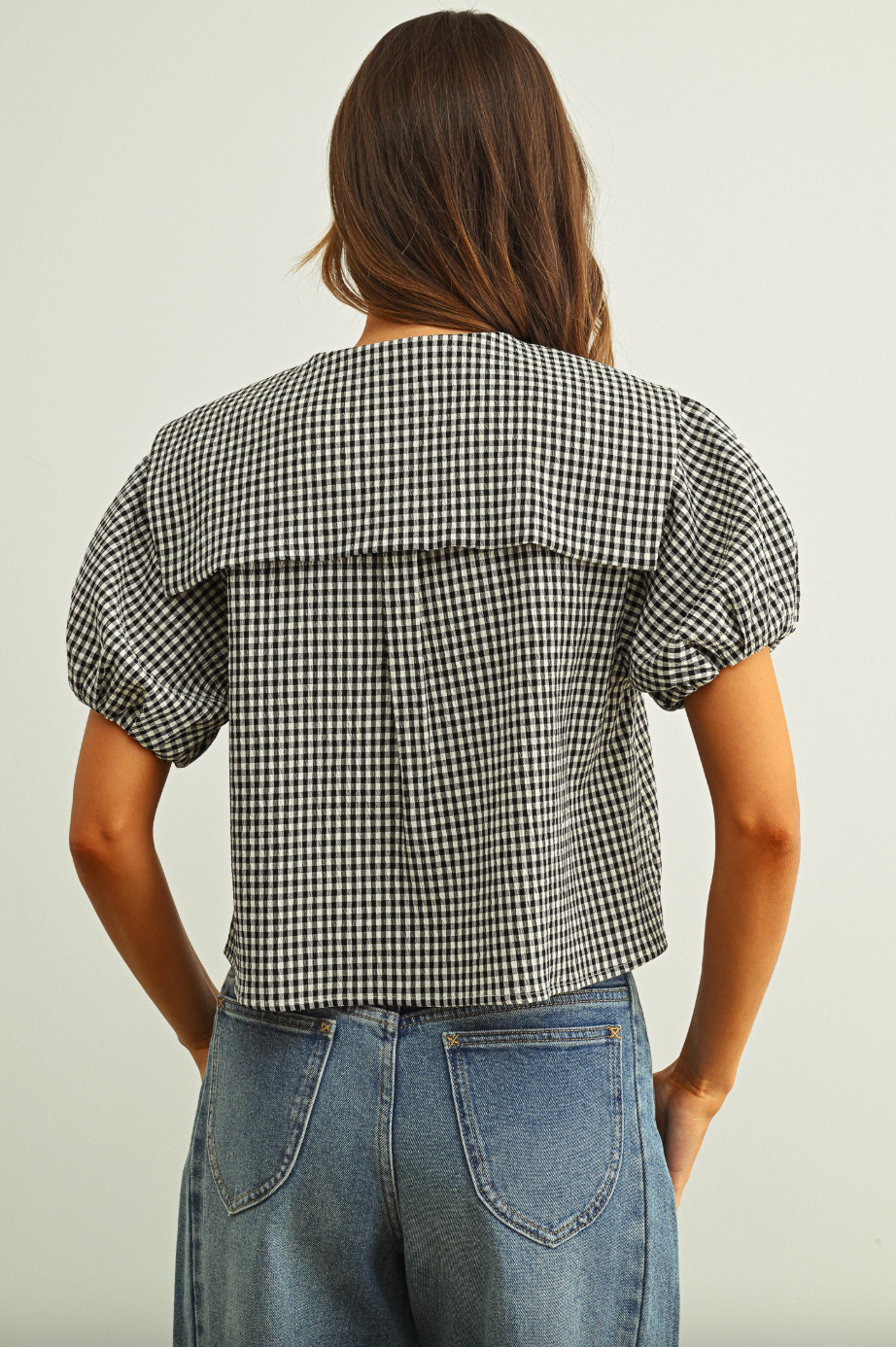 Person wearing a black and white checkered blouse with puffed sleeves on a plain background