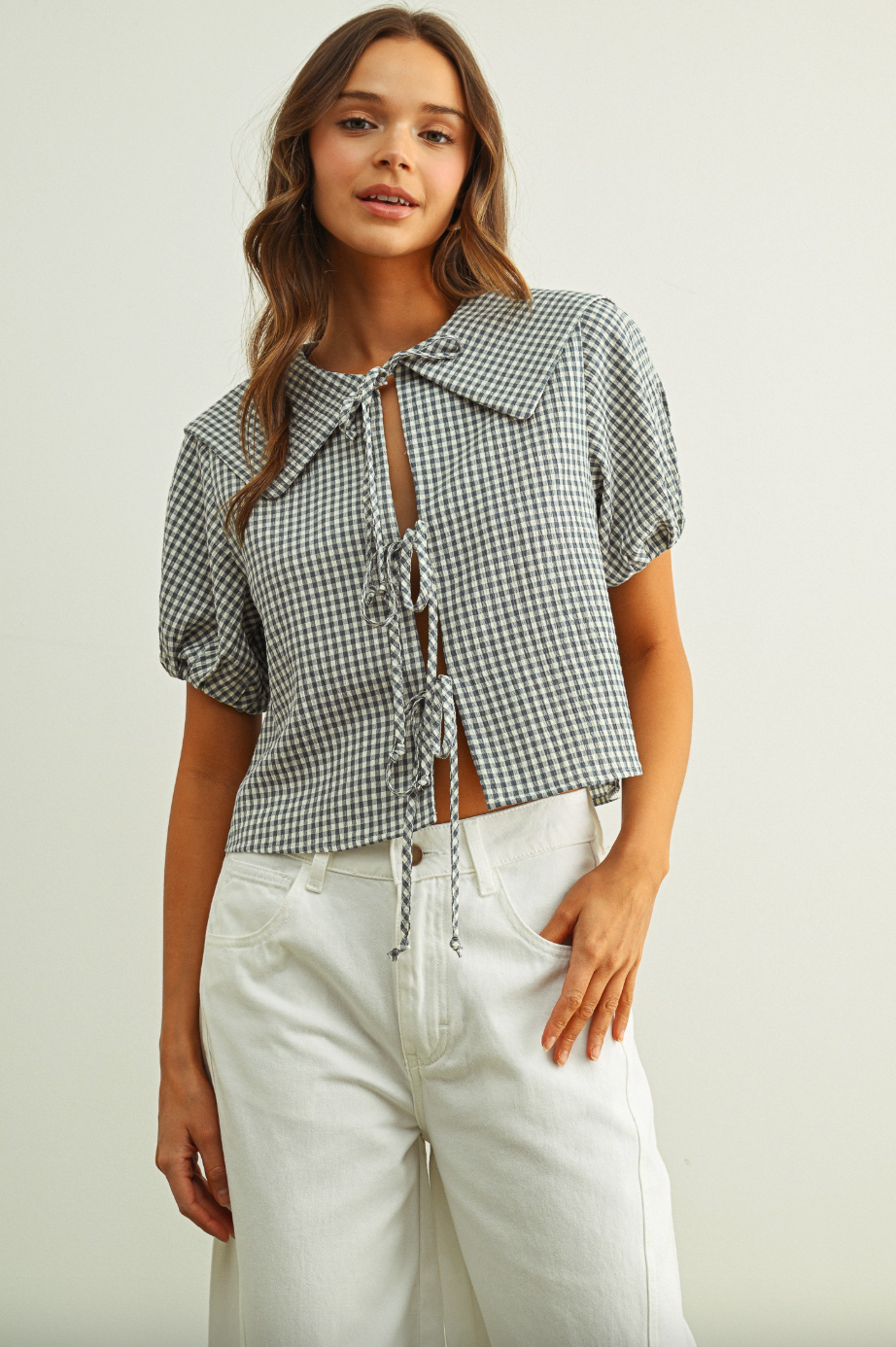 Woman wearing a checkered blouse and white pants on a plain background