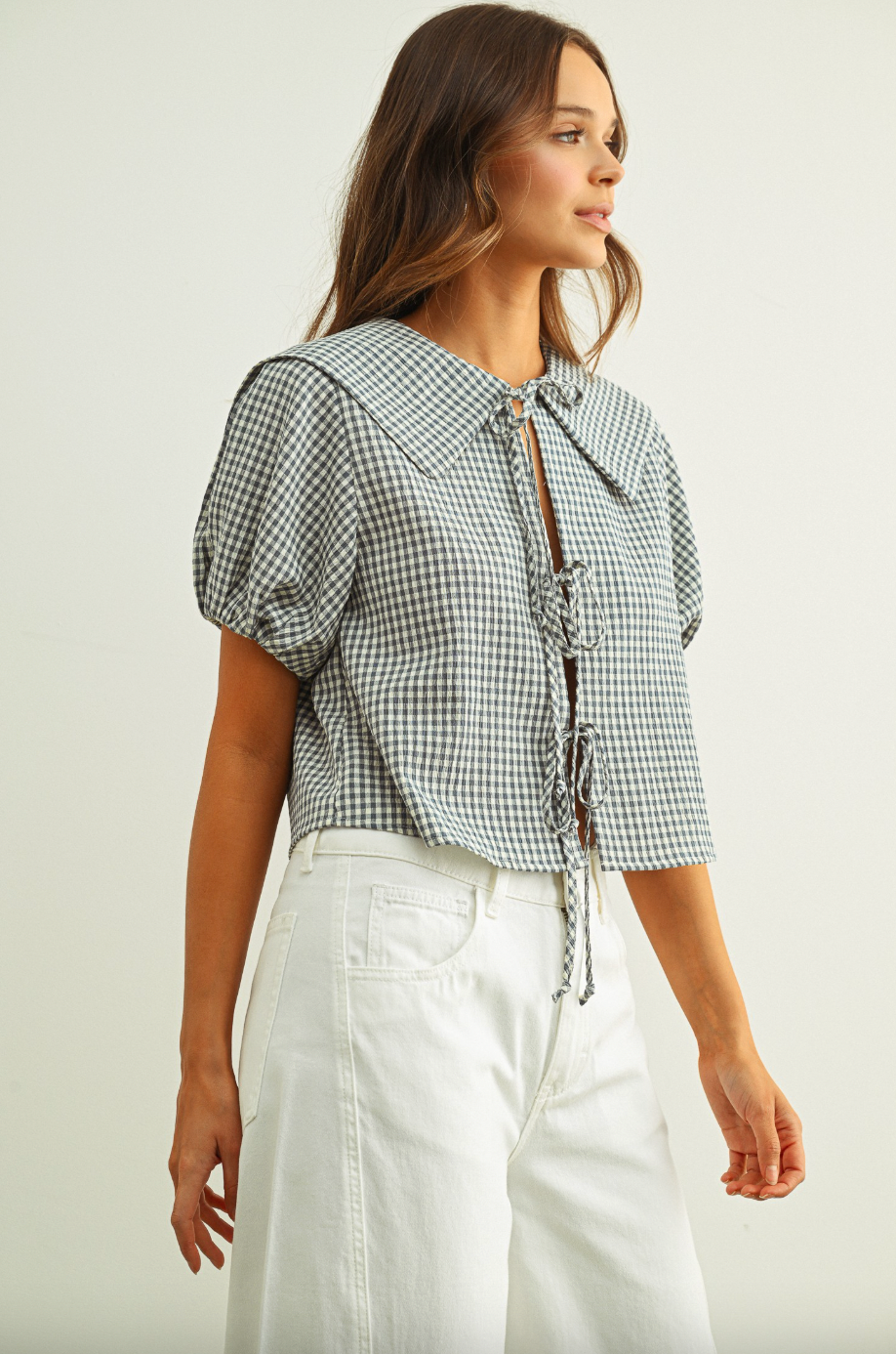 Woman wearing a checkered blouse with puff sleeves and white pants on a plain background