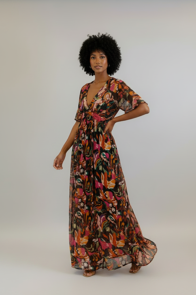 Woman wearing a colorful floral dress against a white brick wall.