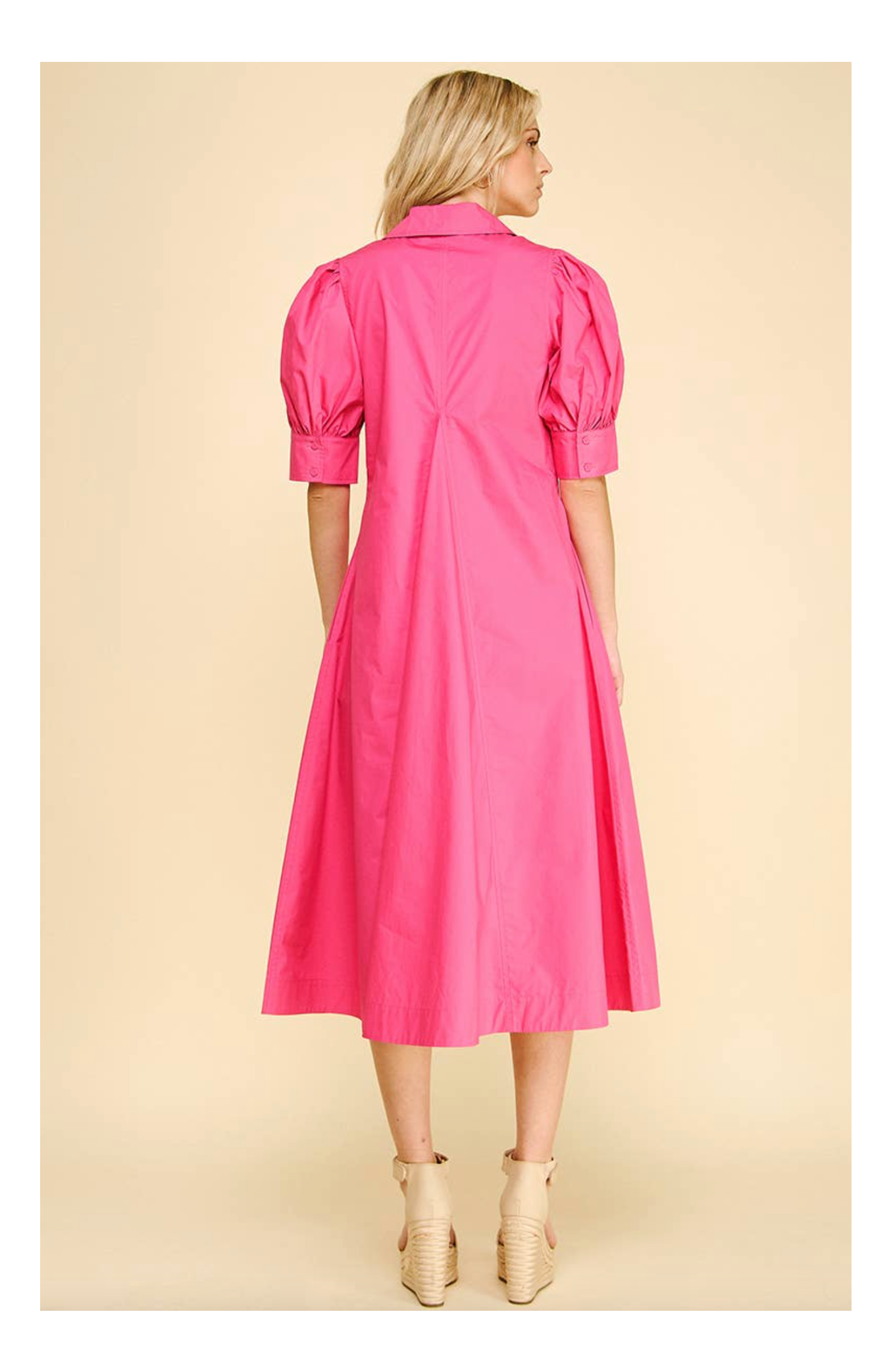 Woman wearing a pink dress with puff sleeves on a beige background