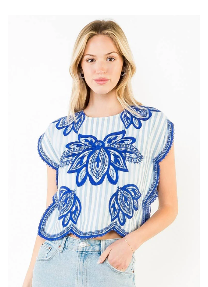 Woman wearing a white top with blue floral patterns and a denim skirt on a white background