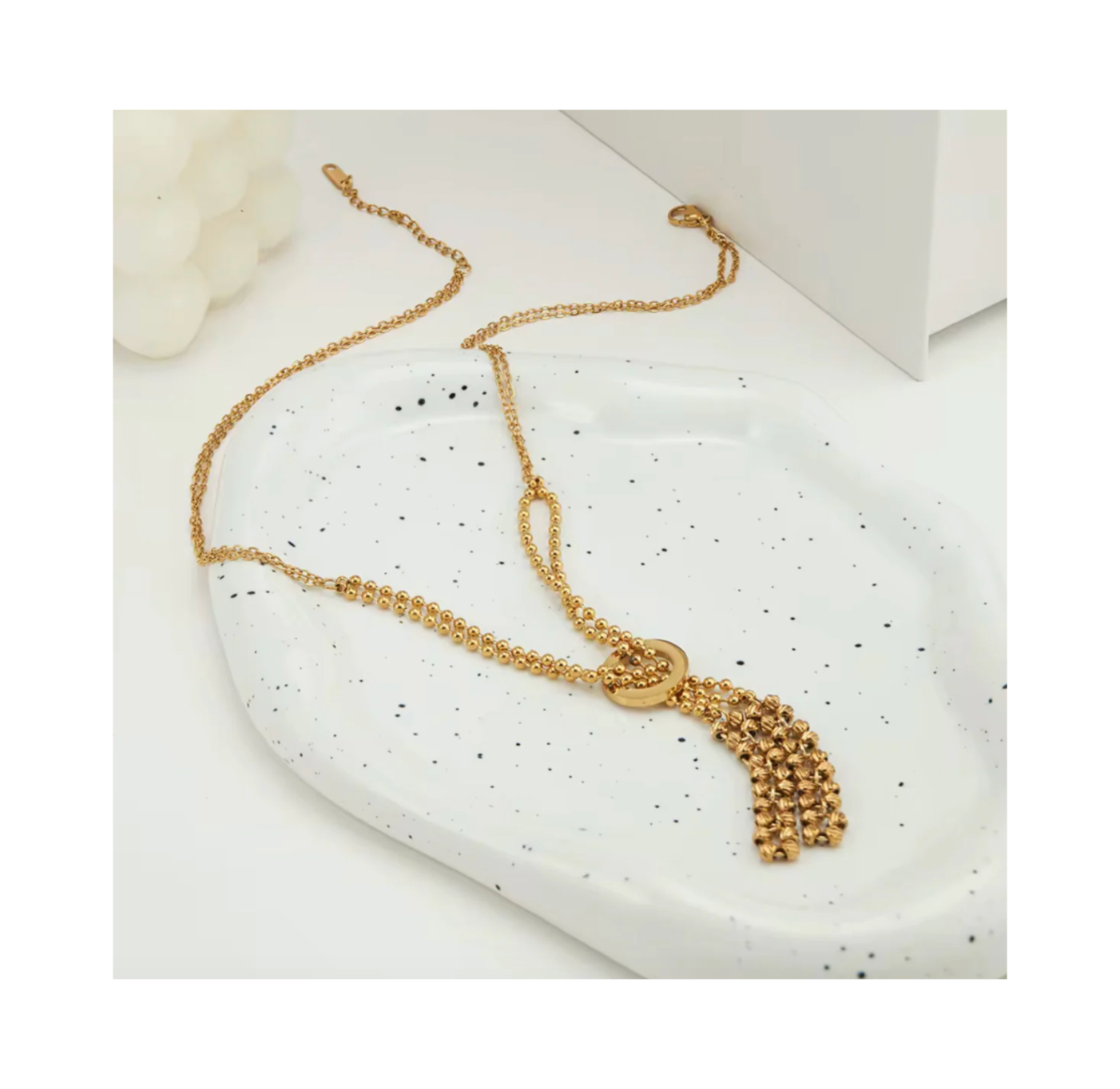 Gold necklace with tassel on a speckled white surface