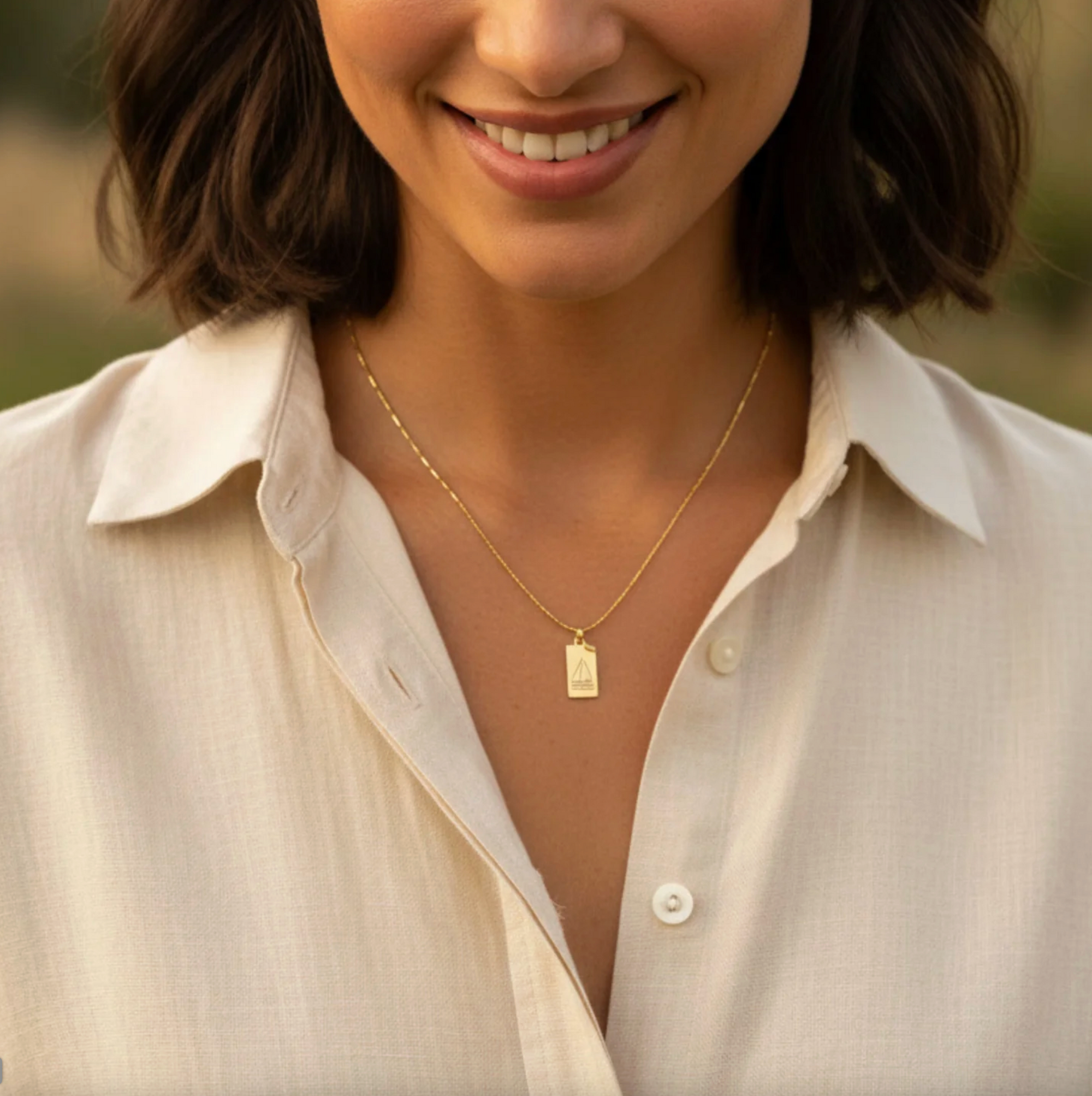Woman wearing a gold necklace with a tag pendant in an outdoor setting