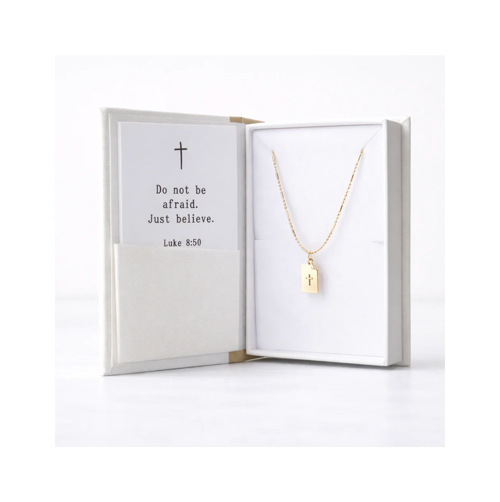 Gold necklace with a tag and cross in an open white box with a inspirational message.
