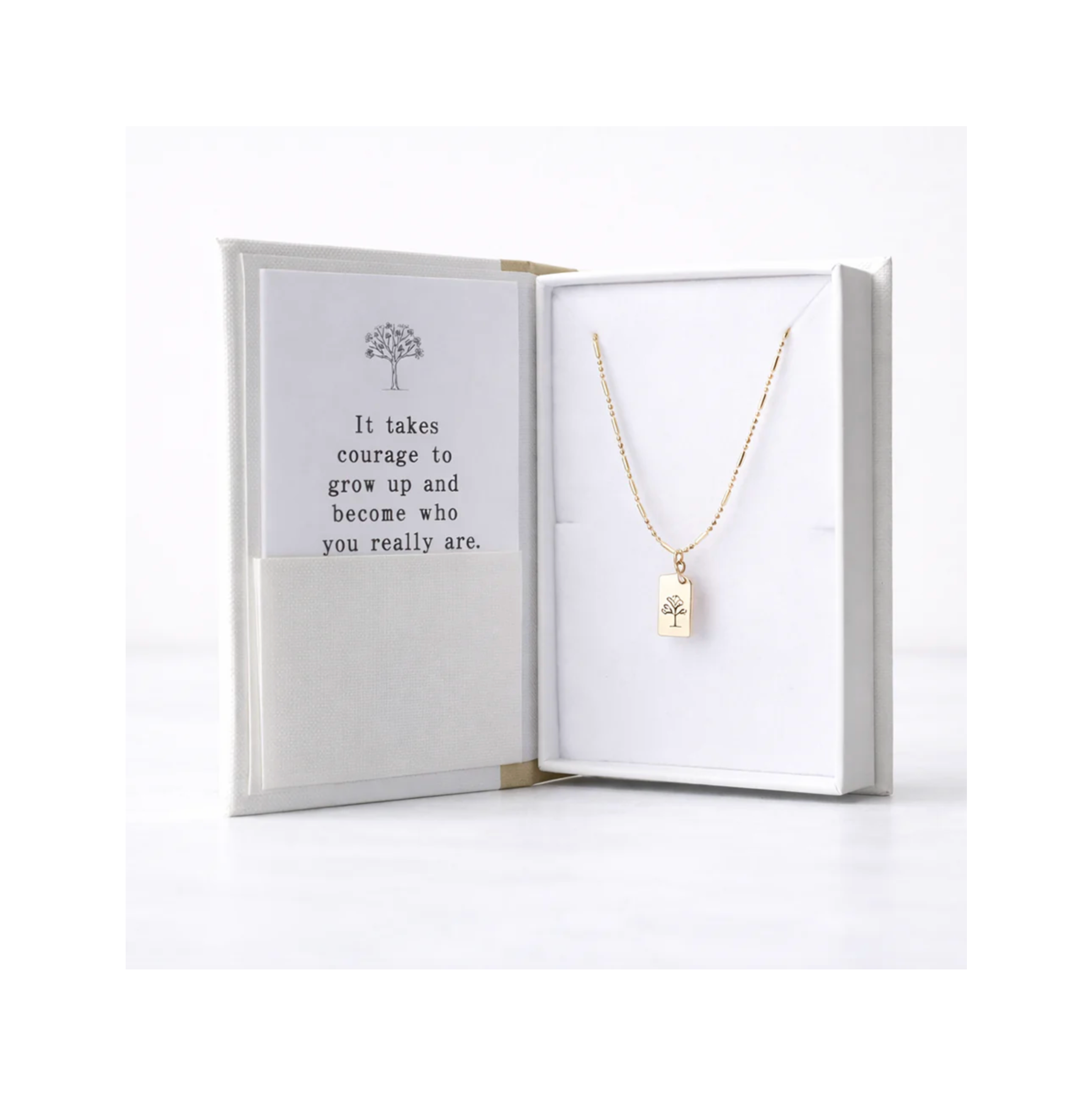 Gold necklace with a tree pendant in an open jewelry box with a motivational quote.