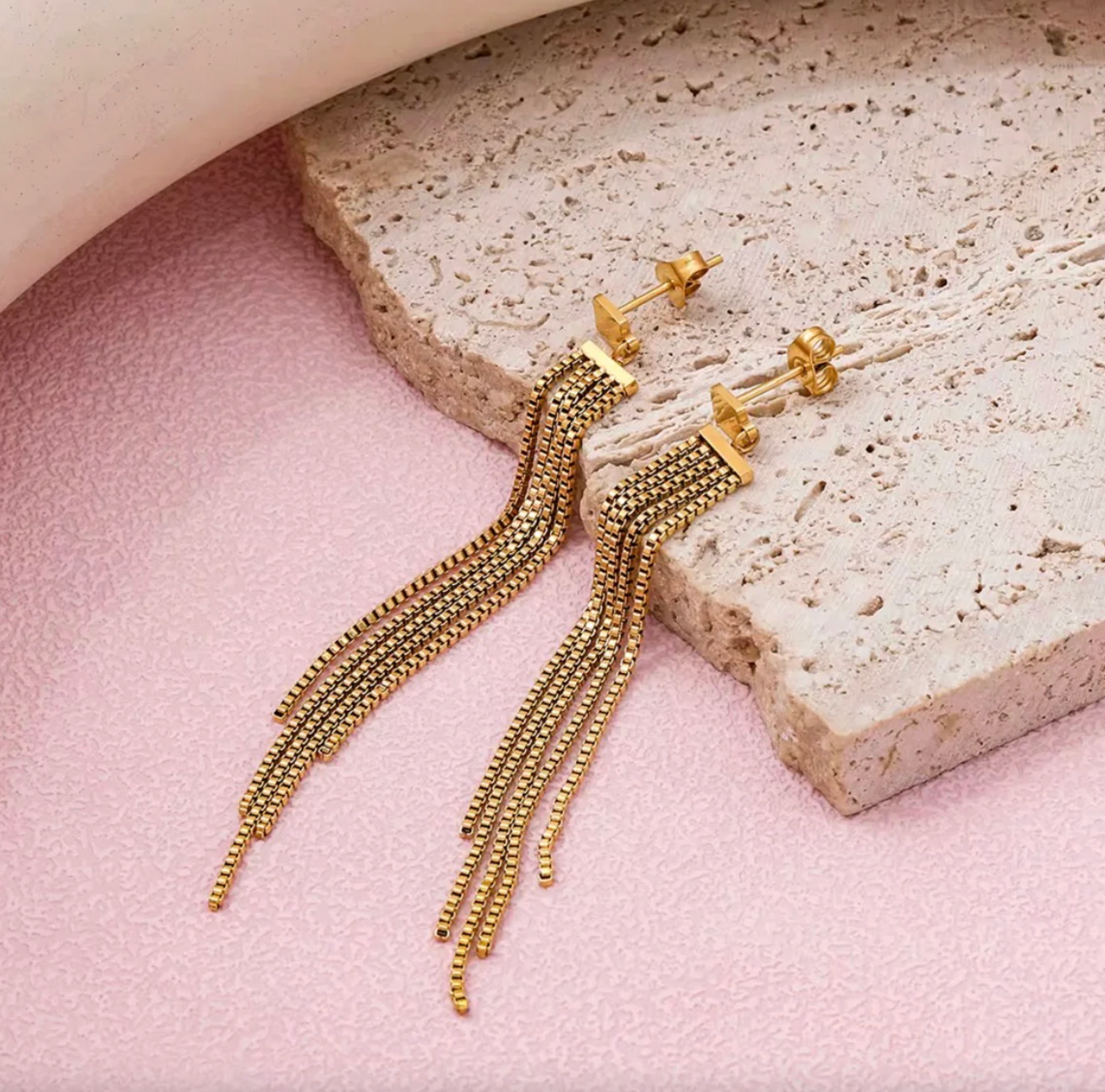 Gold fringe earrings on a pink and beige stone surface