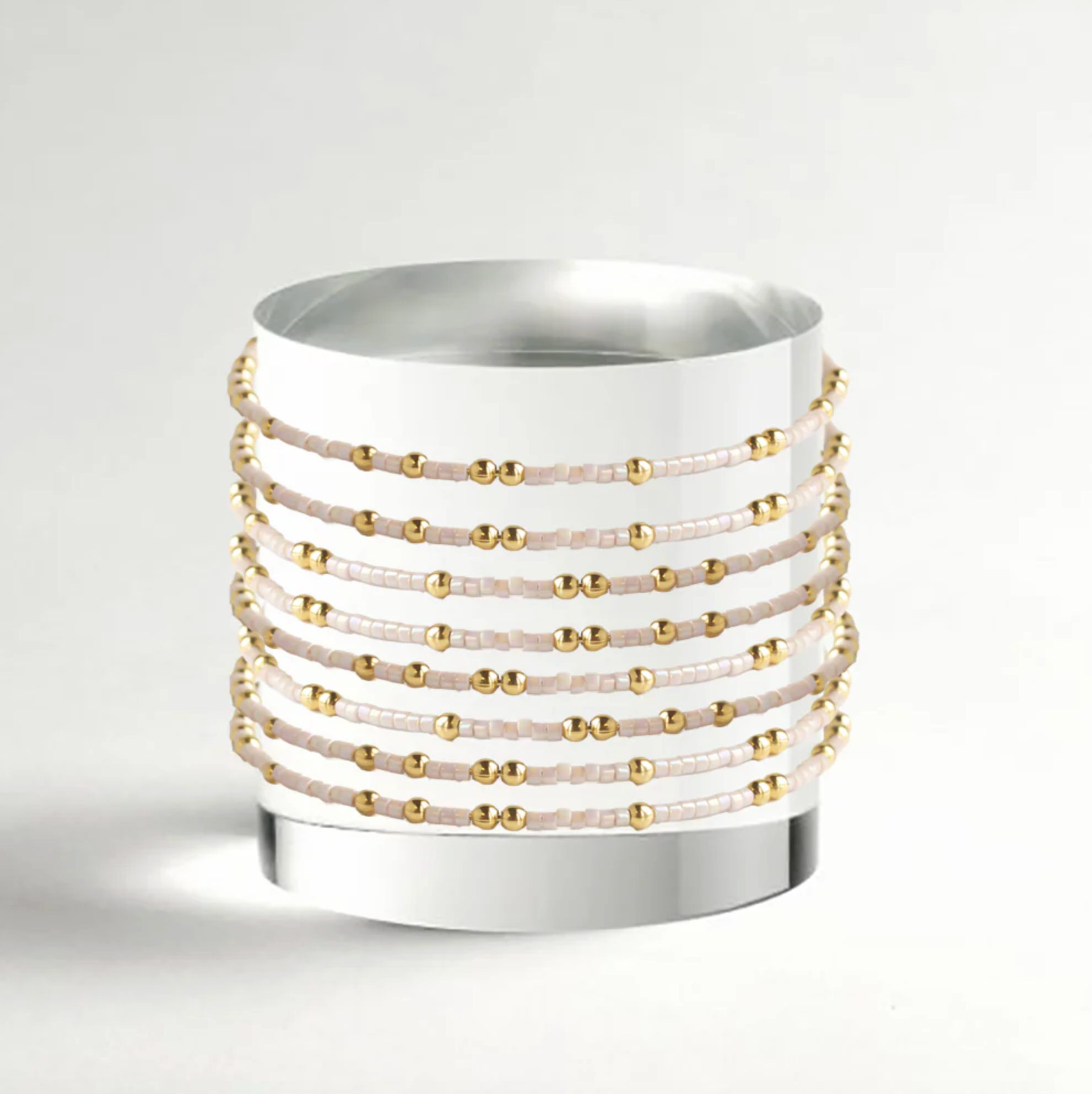 White cylindrical container with gold and beige bead patterns on a light gray background