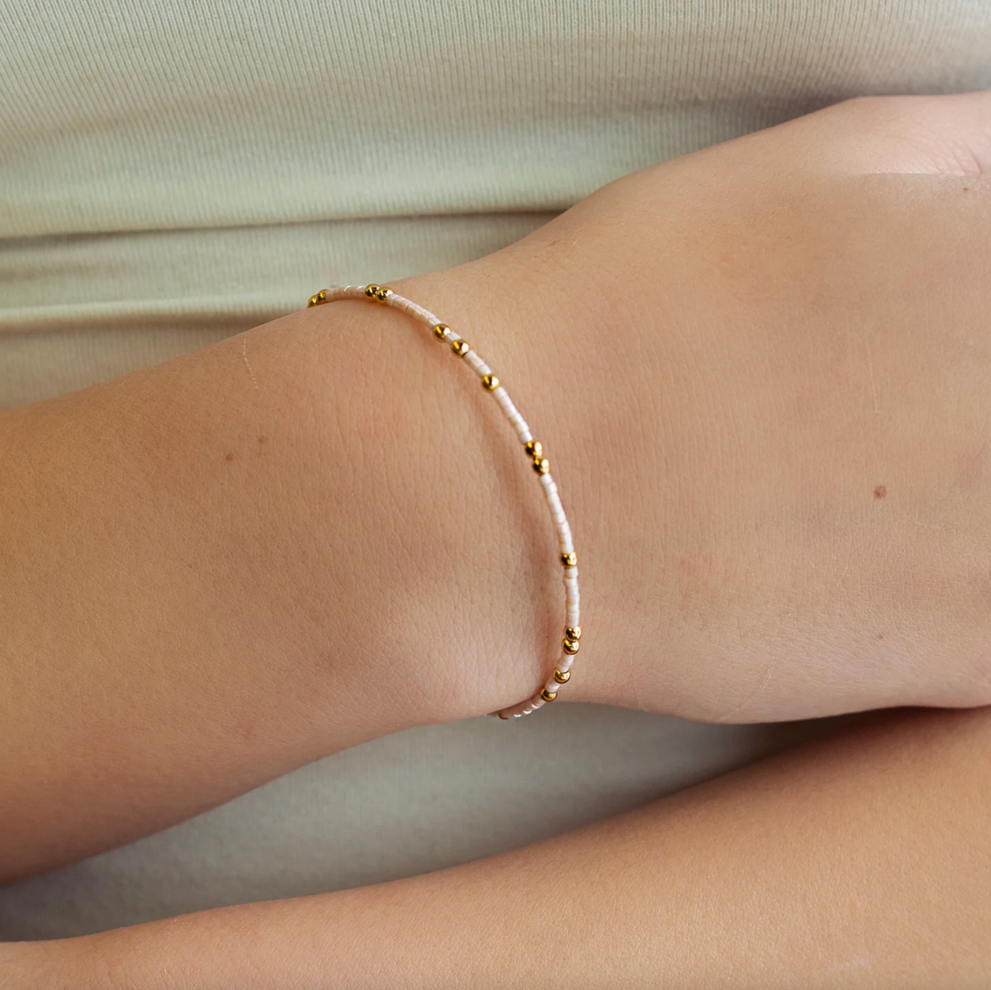 Close-up of a wrist wearing a delicate bracelet with small beads on a neutral background