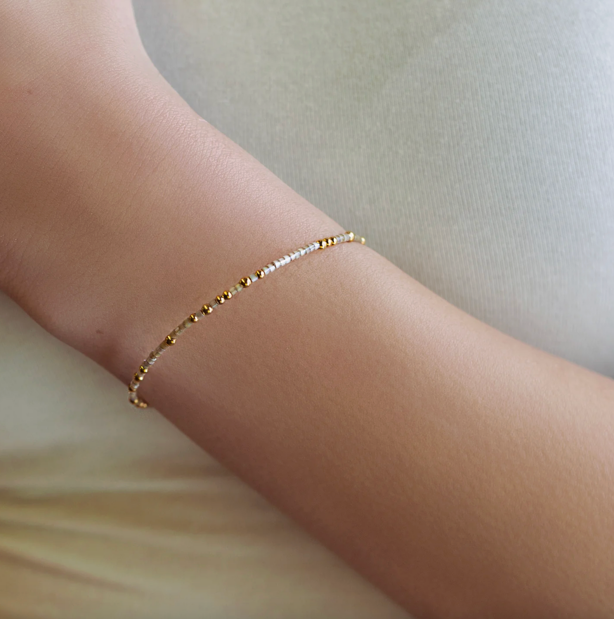 Gold bracelet on a person's wrist against a neutral background