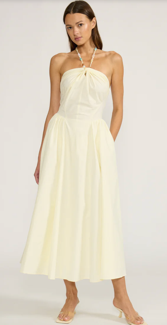 Woman wearing a light yellow halter neck dress on a white background