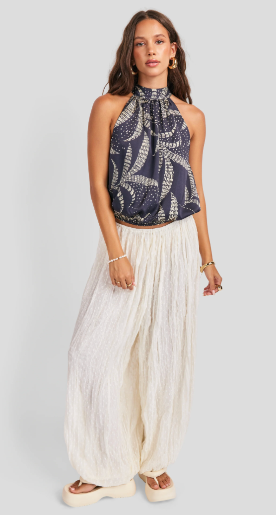Woman wearing a nautical patterned top and white pants on a gray background