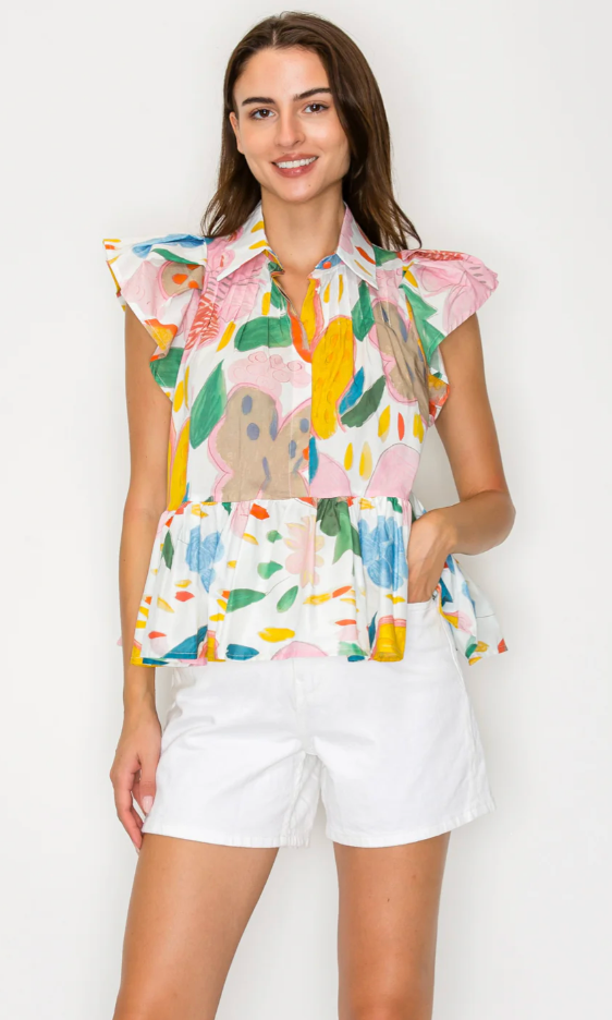 Woman wearing a colorful sleeveless blouse with floral patterns and white shorts on a white background