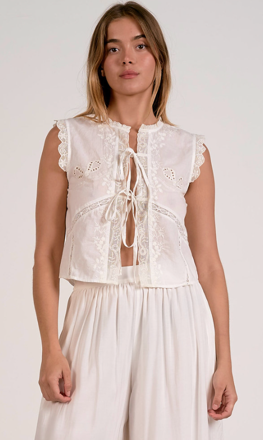 Woman wearing a white lace top and pants against a plain background