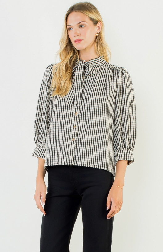 Woman wearing a black and white checkered blouse with puffed sleeves on a white background