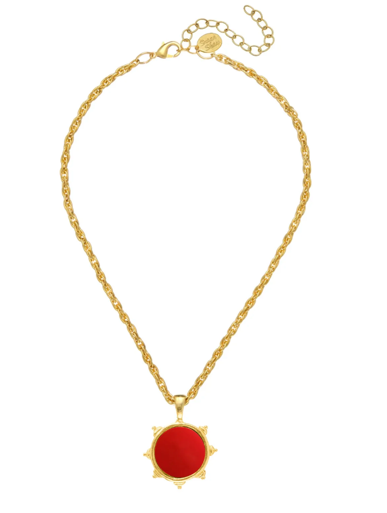 A gold chain necklace with a circular red pendant featuring a sunburst gold border, displayed on a clean white background.