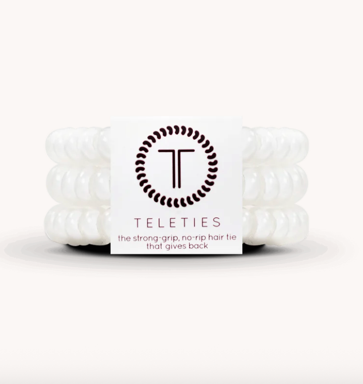 Three white Teleties hair ties stacked behind a white paper label with the Teleties logo and text, photographed on a clean white background.