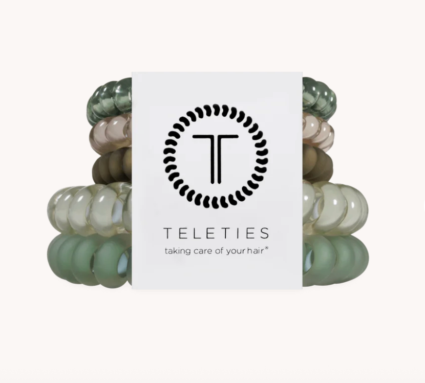 A stack of translucent hair extension or wig bands in muted sage green, gray, taupe, and olive tones, centered behind a white Teleties brand card on a light gray background.