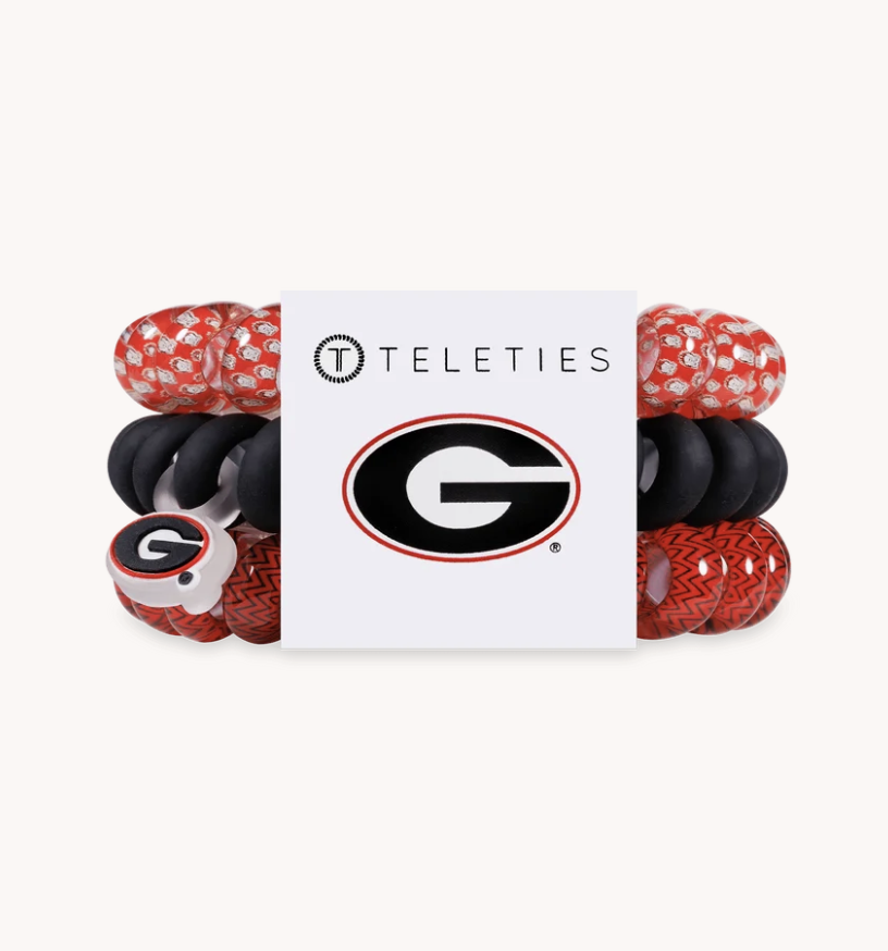 A set of four Teleties baby bracelets featuring the Georgia Bulldogs logo, displayed on a white backing card. The bracelets are arranged in two columns of two, showing red and white patterned silicone, solid black silicone, a red and white patterned charm bracelet, and a red and white patterned bracelet with a large 'G' charm.