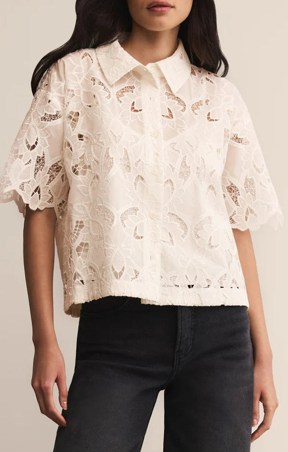 Woman wearing a white lace blouse with black pants on a neutral background